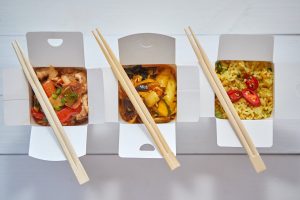 Three take away paper boxes filled with asian food placed in row on white